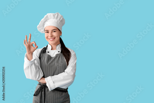 Young female chef showing ok gesture on blue background