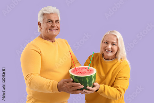 Mature couple with straws in watermelon on lilac background