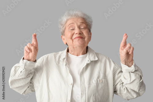 Senior woman crossing fingers on grey background