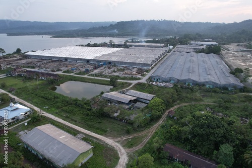 Fotografie Drone panorama showcasing an industrial complex with expansive warehouse roofs, service roads, tropical greenery, and waterfront scenery in a rural coastal region