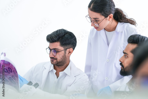 Obraz na płótnie Two lab colleagues holds a petri dish up to the light before monitors showing genetic data while wearing white lab coats and blue protective gloves and modern scientific innovation