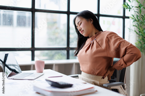 Obraz na płótnie Young woman experiencing back pain and discomfort while working on laptop at desk