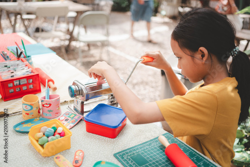 Fotografía Focused Asian kid using a metal rolling machine to flatten polymer clay for art
