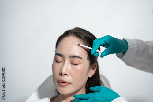 Foto A woman receiving a cosmetic forehead injection from a gloved doctor in a clean clinic, with eyes closed during a beauty treatment