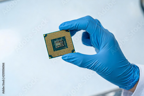 A gloved hand holds a modern semiconductor processor chip, used for electronic engineering and technical research in a clean laboratory setting.