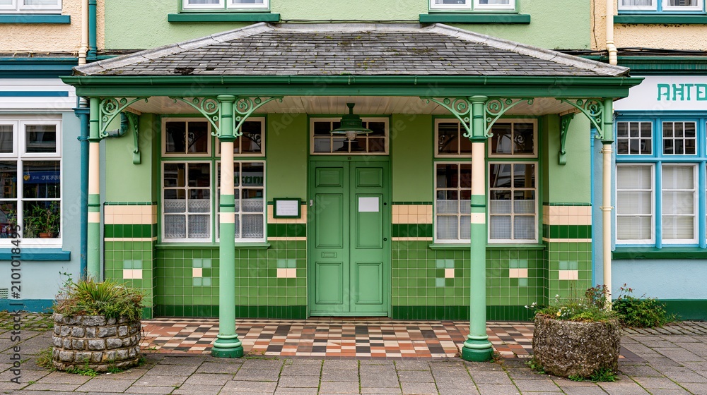 Obraz premium Charming Green Victorian-Style Building Facade with Ornate Porch and Tiled Details