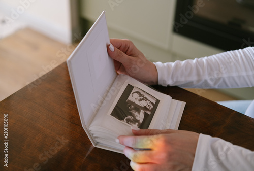 Pregnant woman holding and looking through a photo album filled with cherished family memories while sitting at home. Cozy lifestyle concept representing pregnancy, motherhood, nostalgia, family, love