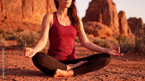 Woman sitting cross-legged on red clay earth with palms pressing into her thighs, grounded and still against a red rock landscape. Earth connection meditation concept