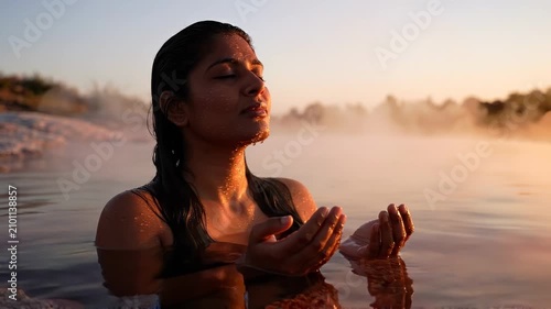 Woman floating in a steaming natural hot spring at dawn with arms extended and eyes closed in total relaxation. Hot spring wellness concept