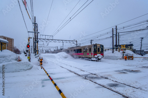 吹雪の中、踏切を駆け抜ける電車