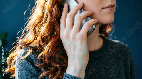 Close up of a curly haired woman holding smartphone to her ear during a phone call.
