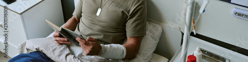 Принти на полотні Header of man resting in military hospital bed, reading book with bandaged arm, representing recovery and patient care