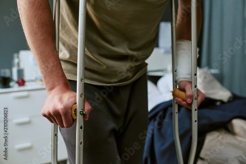 Quadro su tela Close up of unrecognizable man using crutches in military hospital, recovering from arm injury and mobility trauma