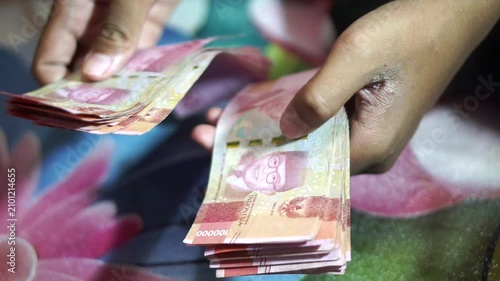 Close-up shot of someone's hands counting a stack of Indonesian Rupiah 100,000 banknotes.