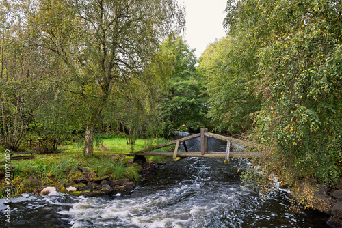 Wooden footbridge over a stream with running water in the summer