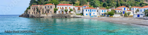 greek village at the edge of  beautiful clear blue water of the sea with white house  in front of green hill  in Peloponnese Greece