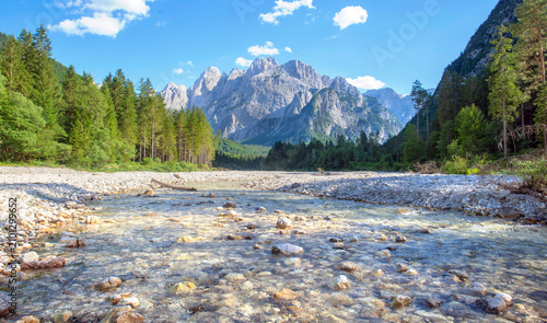 river bed with little water and rocky peak mountains background with hills covered with forest  in italian Dolomites in Malborghetto-Valbruna, Udine province, Italy
