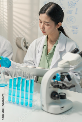 Woman researcher adjusting separating funnel and analyzing test tubes in lab.