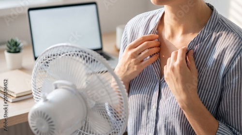 Woman cooling herself with electric fan during hot summer day office work