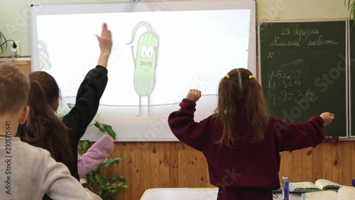 Students participating in a lively interactive lesson by dancing along with a digital character on an electronic whiteboard in a classroom to foster an engaging learning environment