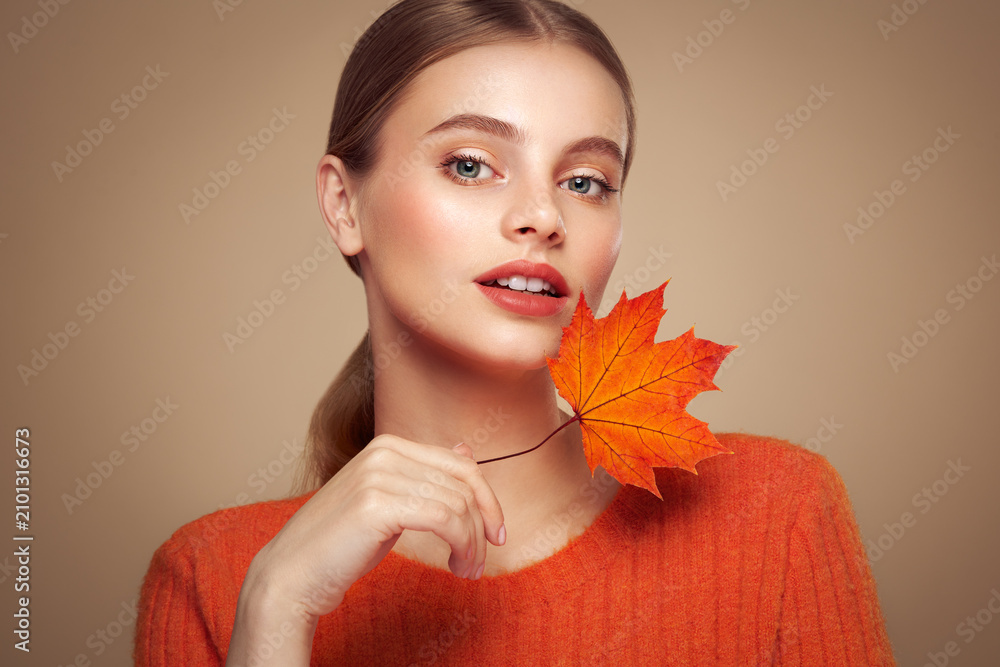 Fototapeta premium Portrait of beautiful young woman in orange blouse with autumn leafs. Healthy clean fresh skin natural make up beauty eyes
