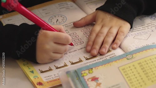 A student writing in a workbook with a red pen to solve math exercises while seated at a desk, conveying academic learning, diligence, and elementary education in a classroom setting