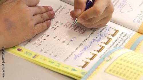 A diligent student completes math exercises in a colorful textbook with a blue pen, representing academic focus, structured learning, and cognitive development in a school environment