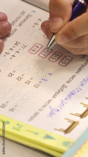 A student using a pen to solve math exercises in a notebook, demonstrating academic focus and elementary arithmetic practice during a session of structured home learning. Vertical