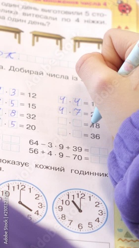 A student using a pen to solve math exercises in a workbook, illustrating the academic process of learning arithmetic and time-telling skills for elementary education. Vertical