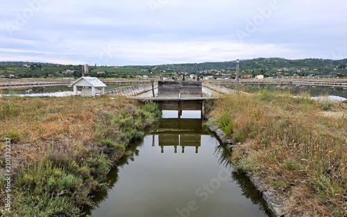 Tableau sur toile Symmetrical reflection of traditional wooden sluice gate in salt pan canal at Se