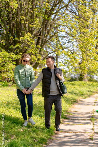 фотографія Happy Mid-Adult Couple Walking and Holding Hands in Green Sunny Spring Park