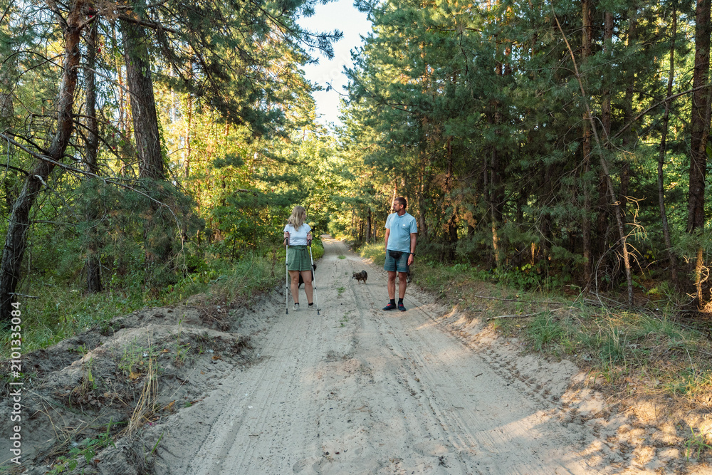 Fototapeta premium Happy Young Couple Hiking with Nordic Walking Poles on a Sandy Trail in Pine Forest