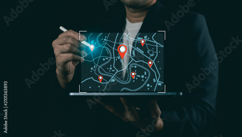 Businessman using stylus pen with glowing digital city map and pin pointers on laptop screen, concept of navigation and logistics tracking.
