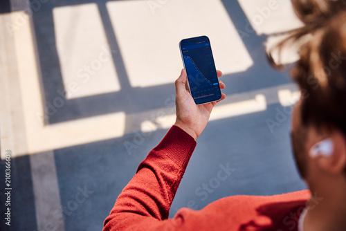Hand holding smartphone with declining stock market chart outdoors