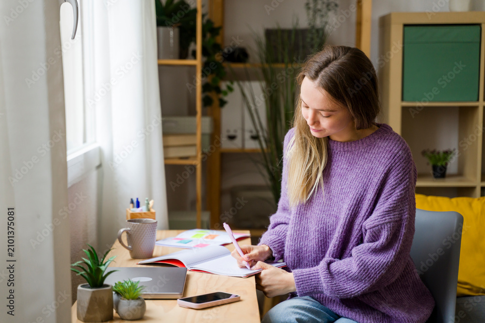© Westend61 - Woman studying and writing in notebook at home with natural light