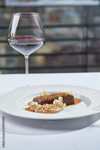 Gourmet roasted meat with mustard seeds, cauliflower, and puree, served with red wine. Elegant terrace fine dining table setting.