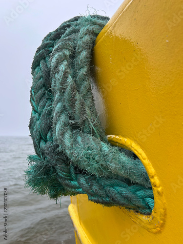 Foto Detailed view of a worn braided mooring rope wrapped around a yellow harbor fixture above the water