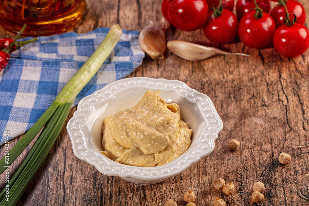 Fototapeta premium Creamy Hummus Bowl with Fresh Ingredients on Rustic Wood Table