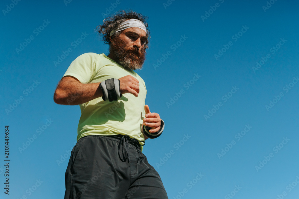 Fototapeta premium Athletic bearded man running with wrist weights outdoors