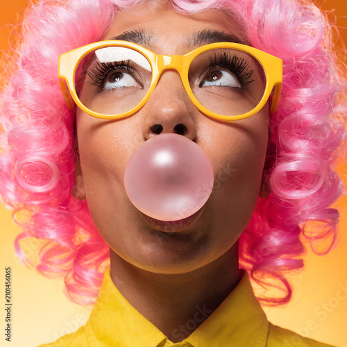 Person Blowing Bubble Gum Wearing Pink Wig and Colorful Glasses