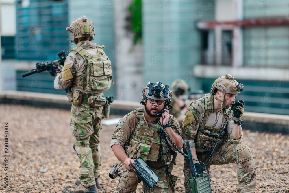 Fototapeta premium Military tactical team reviews mission plan on rugged laptop during outdoor field briefing