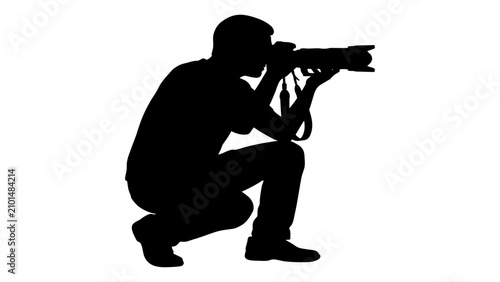 Bild auf Leinwand Photographer crouches while holding a camera to capture a subject in this black silhouette