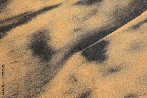 Abstract patterns of black and golden beach sand shaped by wind and waves, creating a striking natural texture and coastal background.