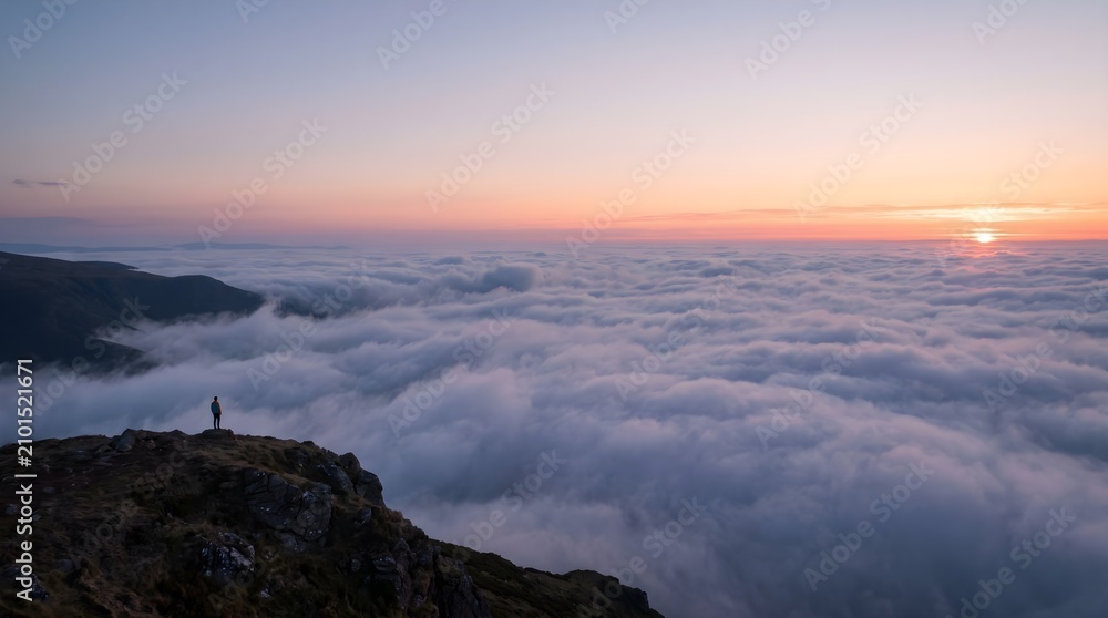 Obraz premium Person standing on mountain peak above clouds. Hiker watching sunset over valley landscape.