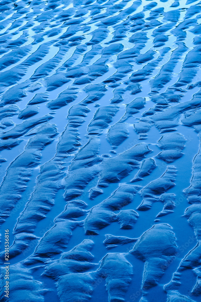 Obraz premium Abstract pattern of blue sand ripples created by the tide on a wet beach. Natural texture with flowing lines, ideal as a background or design element.