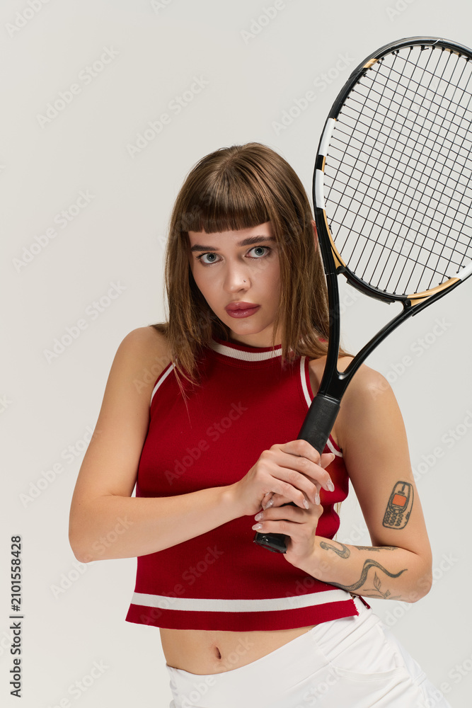 Fototapeta premium Stylish young woman embodies retro tennis vibes in grey studio
