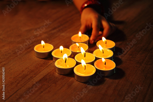 Fotografía Hands arranging lit tealight candles on a wooden table creating a warm and peace