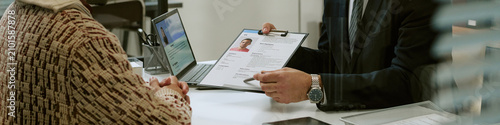 Header of Man Interviewing Young Adult Man Reviewing Resume in Office