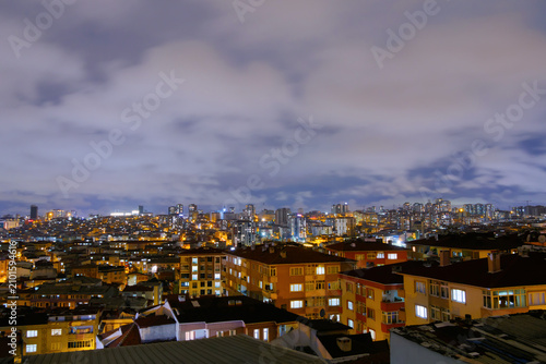 View of clouds in the dark sky over cityscape with typical turkish apartment, residential buildings with warm illumination and illuminated windows in Istanbul, Turkey at night