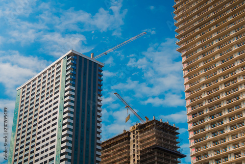 View of two yellow tower cranes and unfinished building construction against blue sky with clouds in Batumi. Urban, engineering, developing and industrial concept